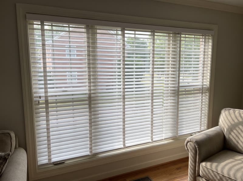 White 2.5 inch faux wood blinds half tilted on a living room window in an Alpharetta brick colonial
