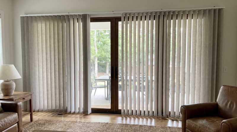 Greige vertical blinds half rotated across a sliding patio door in a Woodstock farmhouse