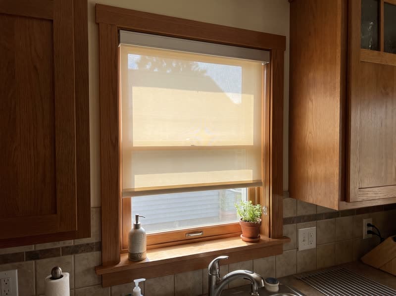 Cream roller shade half raised above a kitchen sink in a Roswell craftsman home