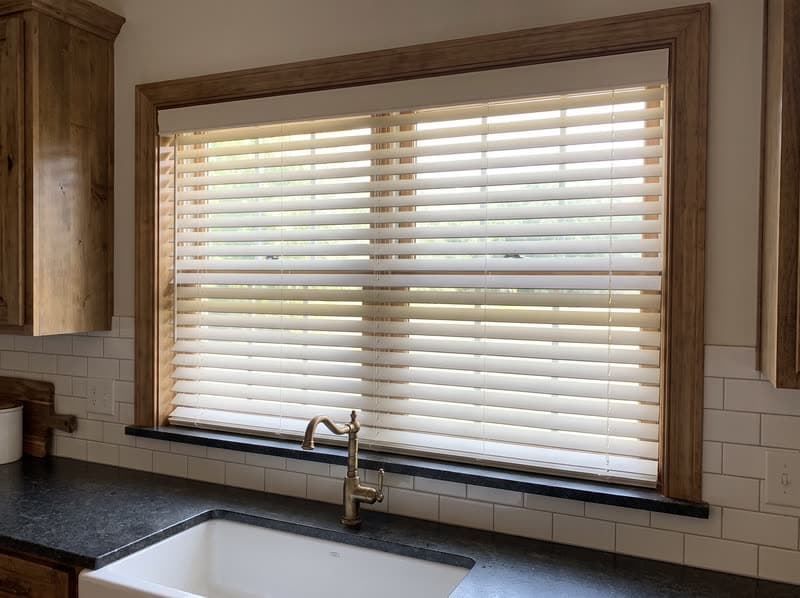 White faux wood blinds tilted closed over a kitchen sink window in a Milton farmhouse
