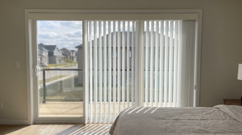 White vertical blinds drawn two thirds across a bedroom slider in Cumming