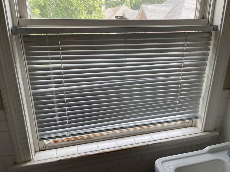 Brushed aluminum mini blinds tilted closed on a bathroom window in Duluth